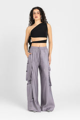 Woman wearing a black one-shoulder top and gray cargo pants on a white background