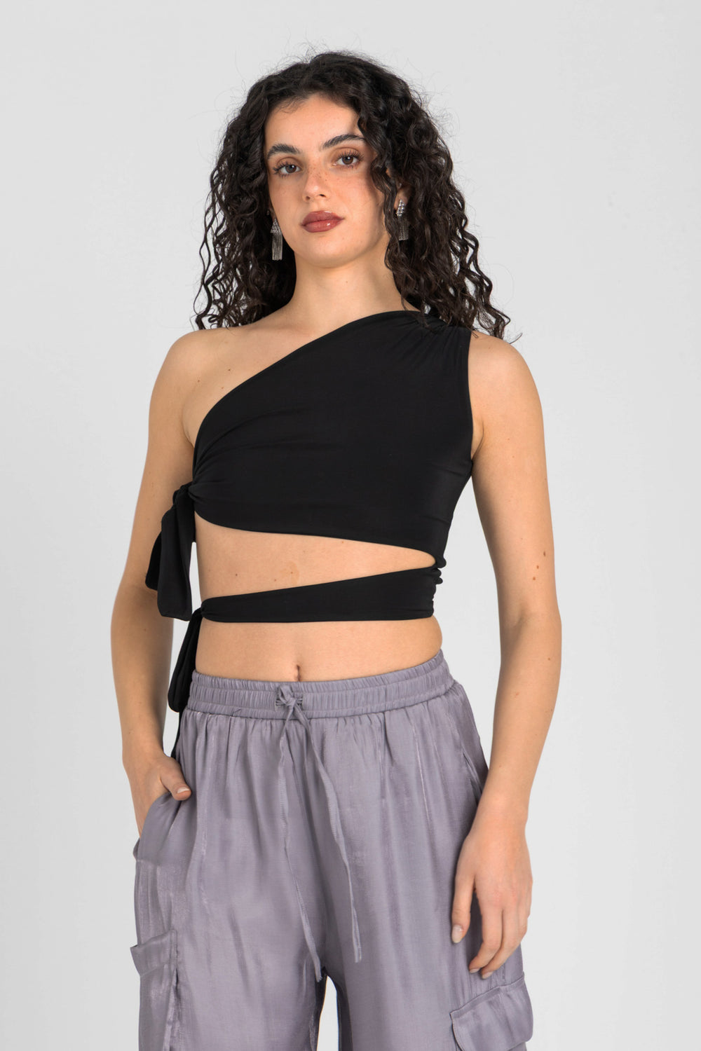 Woman wearing a black one-shoulder top and gray pants on a light gray background