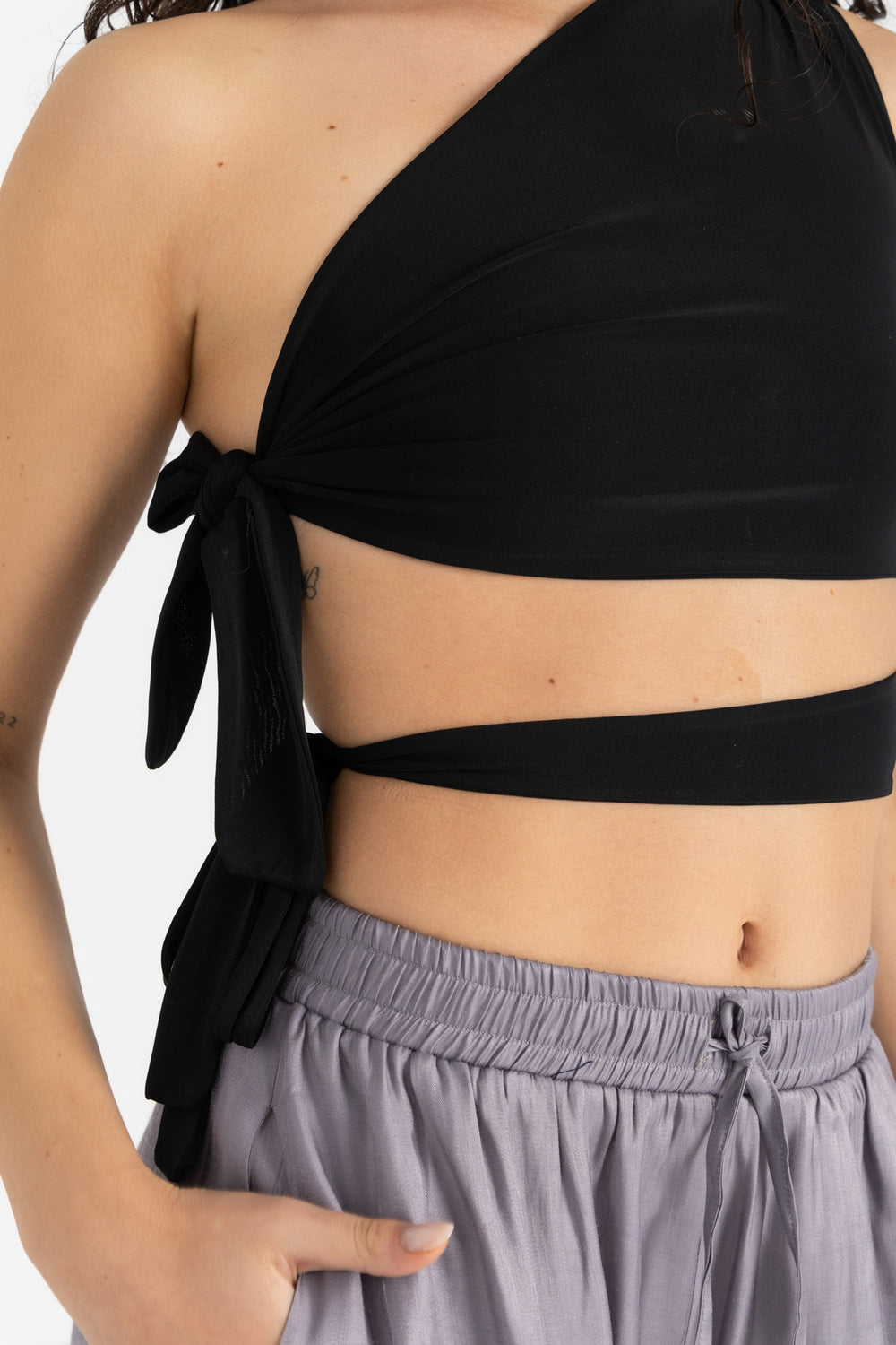 Person wearing a black halter top and gray pants on a white background