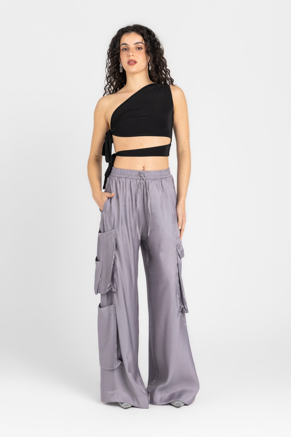 Woman wearing a black one-shoulder top and gray cargo pants on a white background