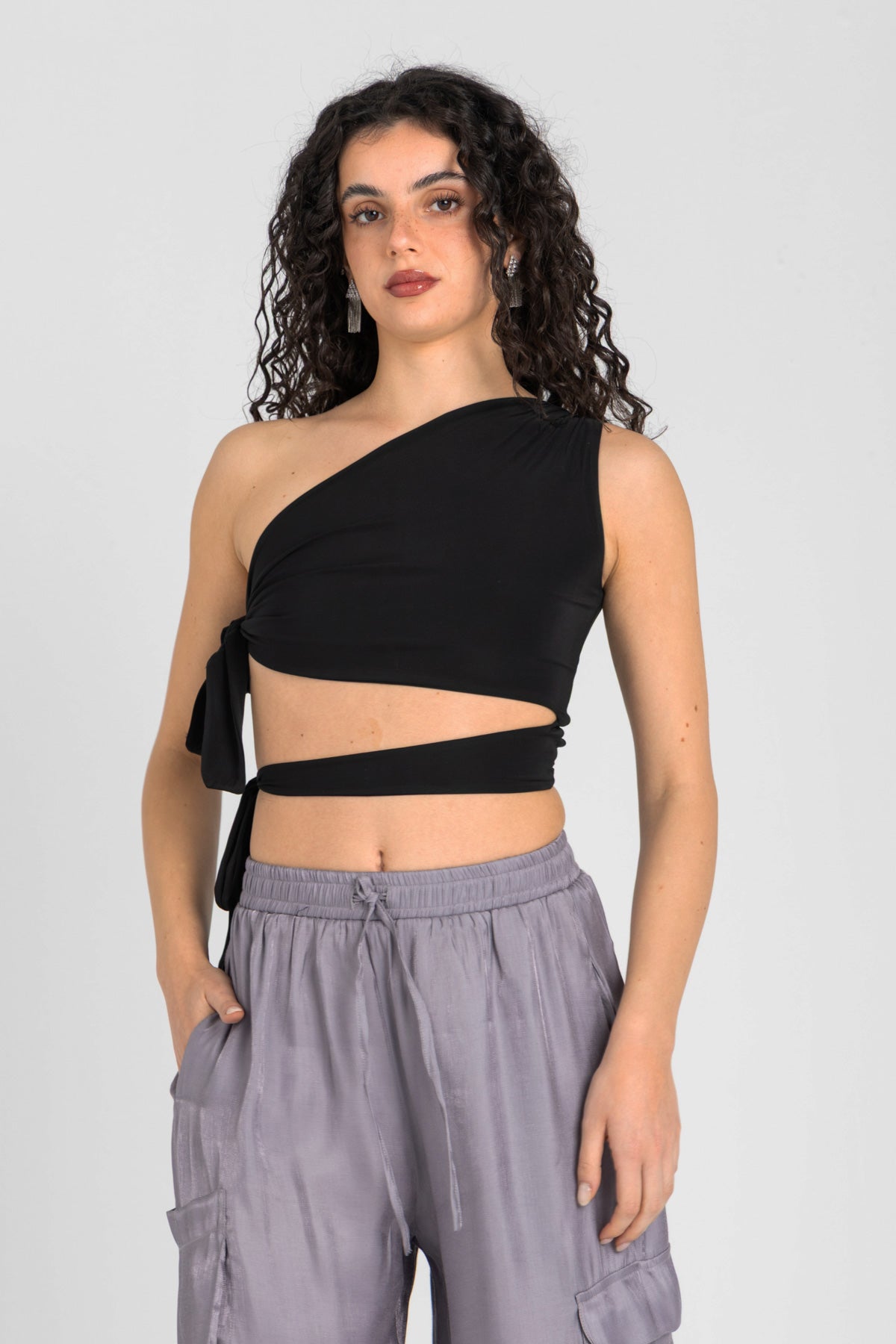 Woman wearing a black one-shoulder top and gray pants on a light gray background