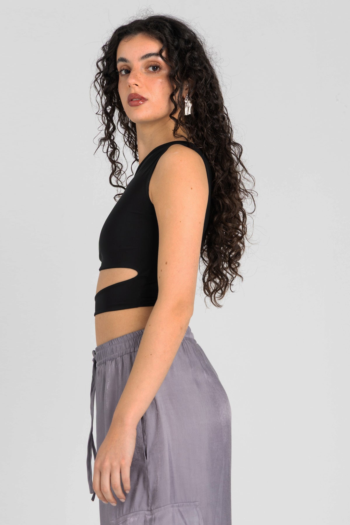 Woman wearing a black sleeveless top with cut-out design and gray pants against a plain background